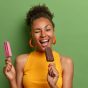 joyful-curly-haired-woman-bites-delicious-ice-cream-winks-eye-has-fun-happy-expression